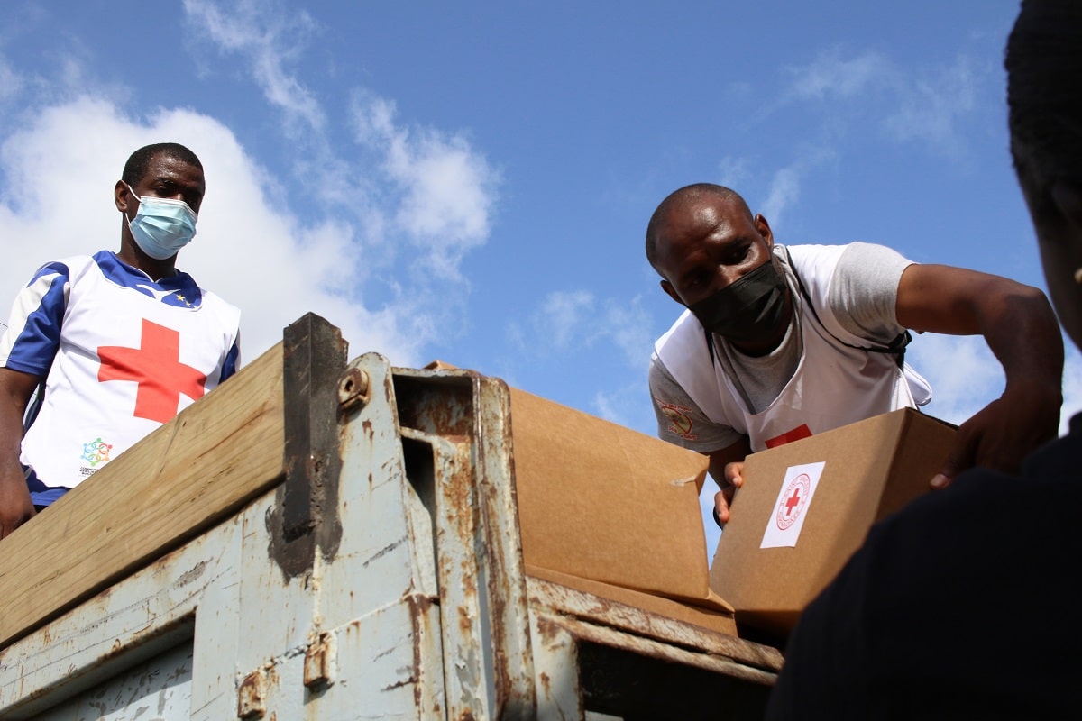 Two men in masks are distributing boxes from the back of a truck.
