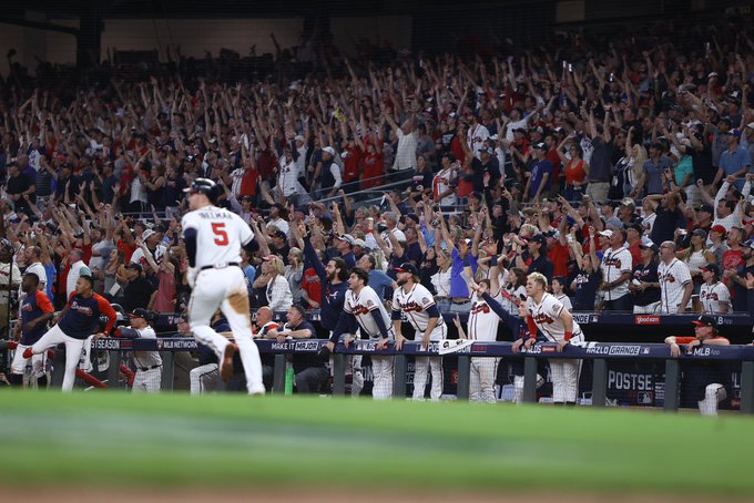 Freddie Freeman runs toward first base as the crowd in the stands at Truist Park and Freemanâ€™s teammates in the dugout all watch his home run sail out of the ballpark and begin to celebrate with their arms raised in the air.