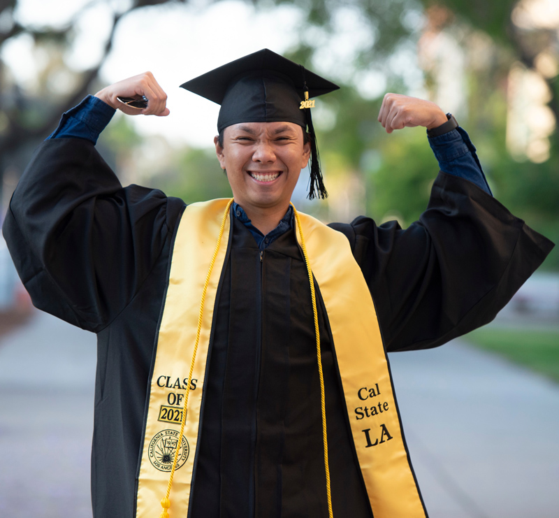 a person wearing a graduation cap and gown flexing their bicep muscles and smiling