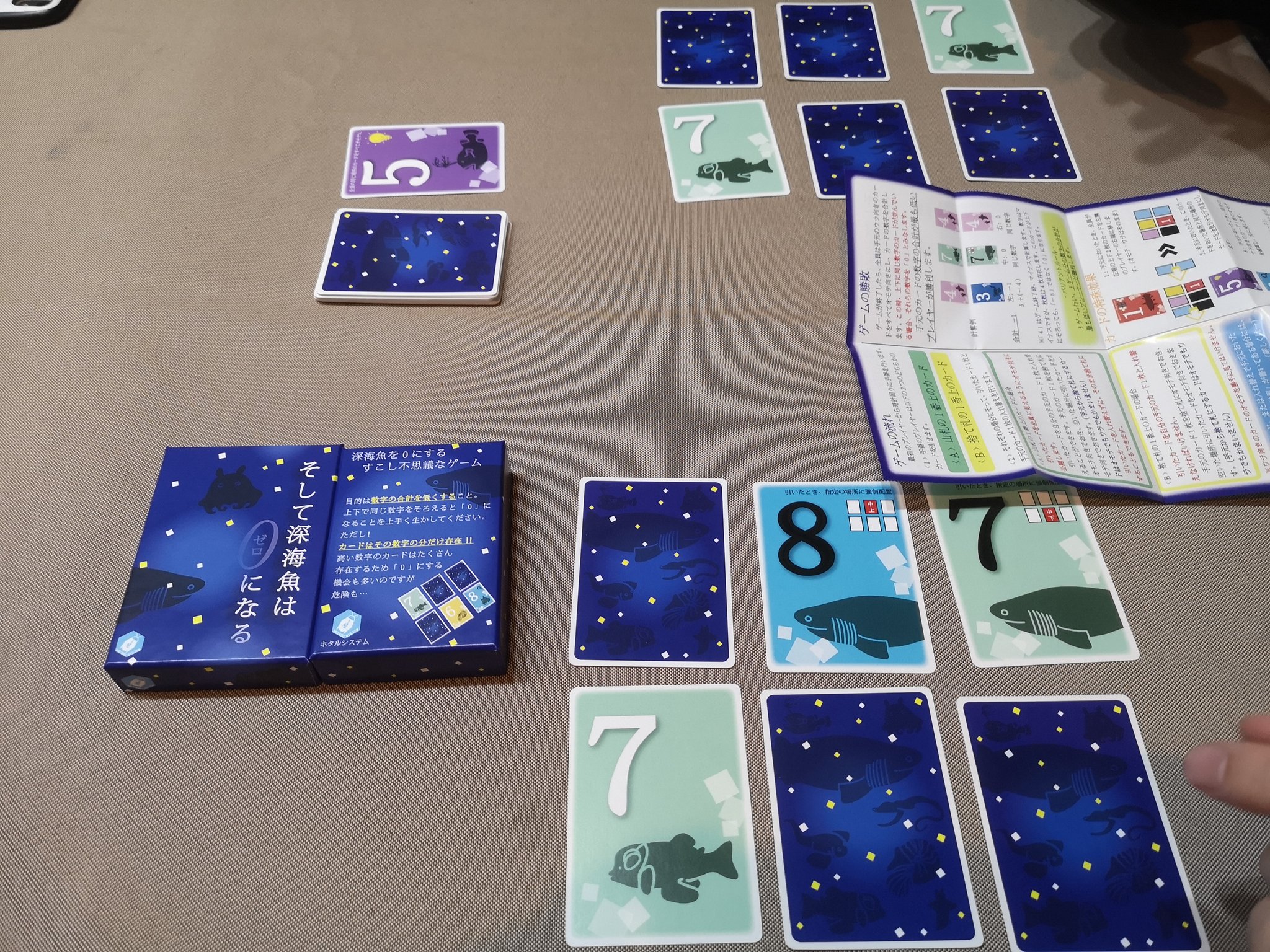 おやつアンドロメダ そして深海魚は0になる 終了タイミングで手元のカード合計が最も低いと勝つ やることは山札か捨札から引いて置くだけ 置いたときに効果が起動し カードの効果でインタラクションが設計されてる すぐに遊べてルールがシンプル