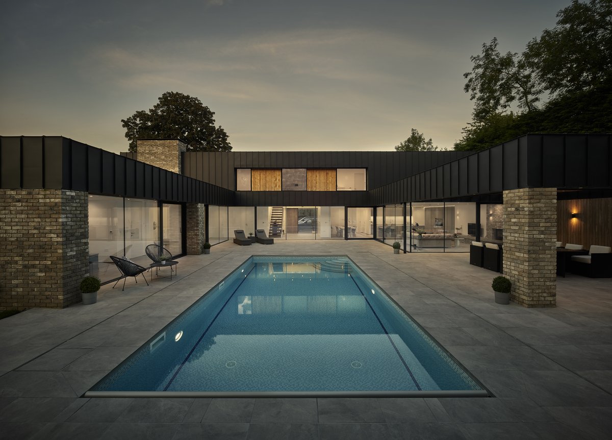 A photo of our recently completed Gowland House project looking back towards the vaulted entrance hallway, constructed by S Voase Builders. Frameless glass wraps around the open plan kitchen, dining and living area which provides views onto the courtyard and outdoor swimming pool