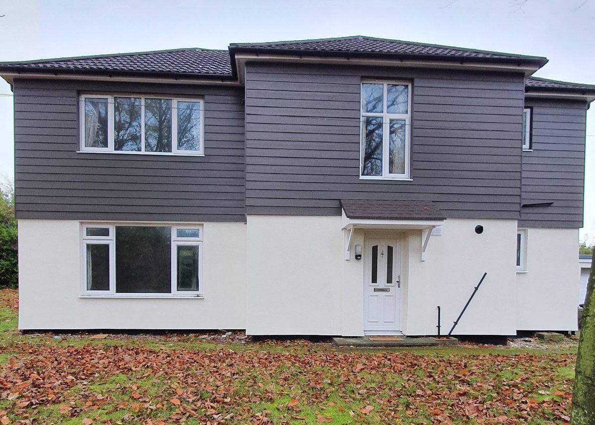 A house with a white ground floor and a first floor clad in what looks like dark grey wood. It looks clean and new. 