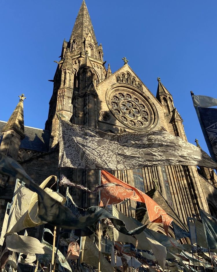 A tall cathedral spire against blue sky with silk pennants fluttering in the foreground