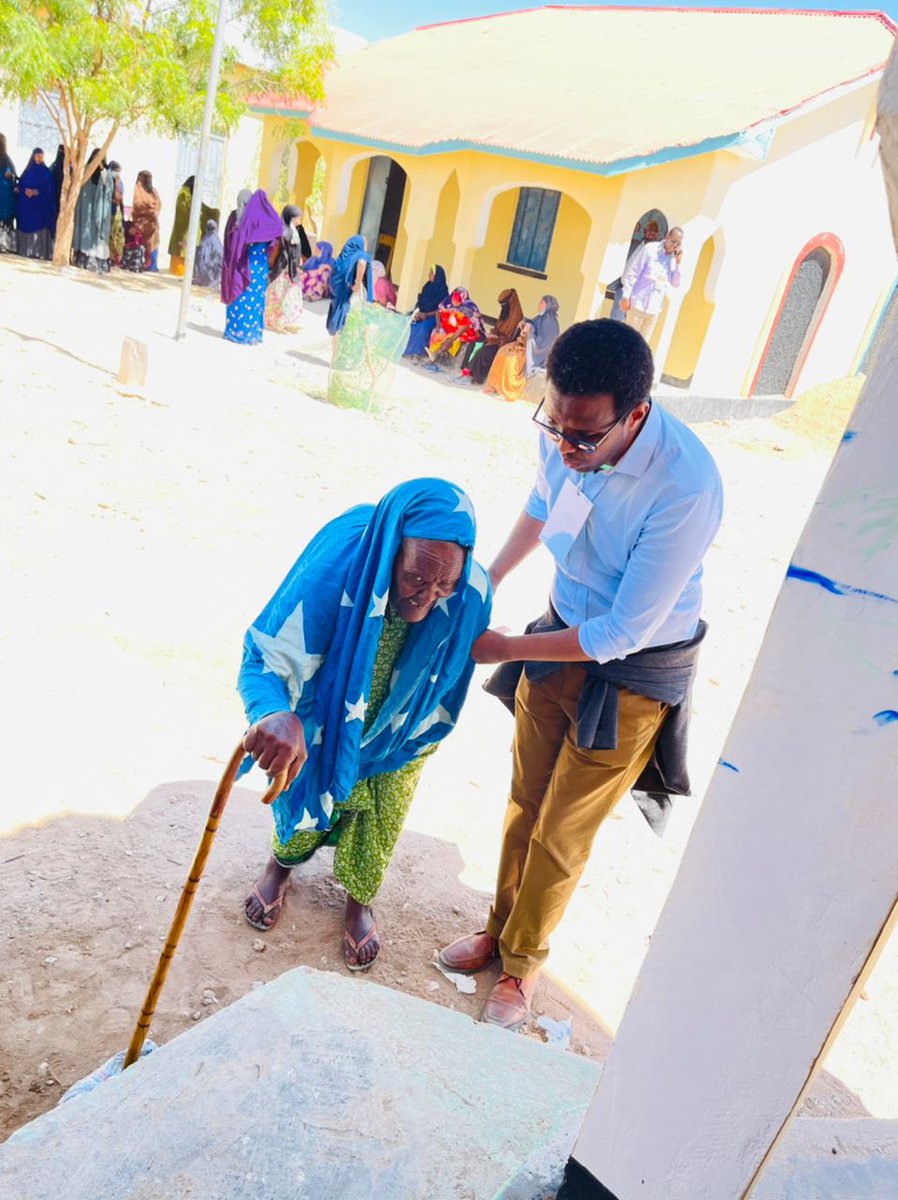 An elderly woman is helped by <a href="/ASalwe/">Abdusalam Salwe</a> at a voting centre in Qardho to cast her ballot. She is a wearing a scarf made of in the colour of Somali national flag. #PuntlandElections #Somalia
