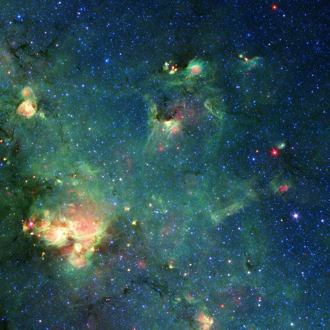 Green and blue gases from a nebula overtake this image. The top right of the image has bright spots of stars that resemble the eyes and snout of Godzilla. At the bottom left is a bright spot that could be perceived as fire from the fictional monster.