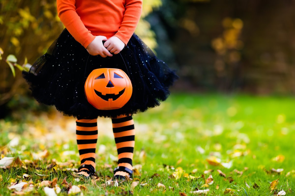 Girl dressed for halloween holding a bucket that looks like a jack-o-lantern