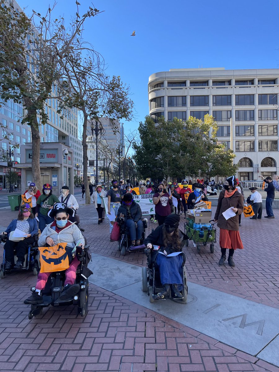 A group of people march down a busy street, the march is led by 4 people who are seated in wheelchairs