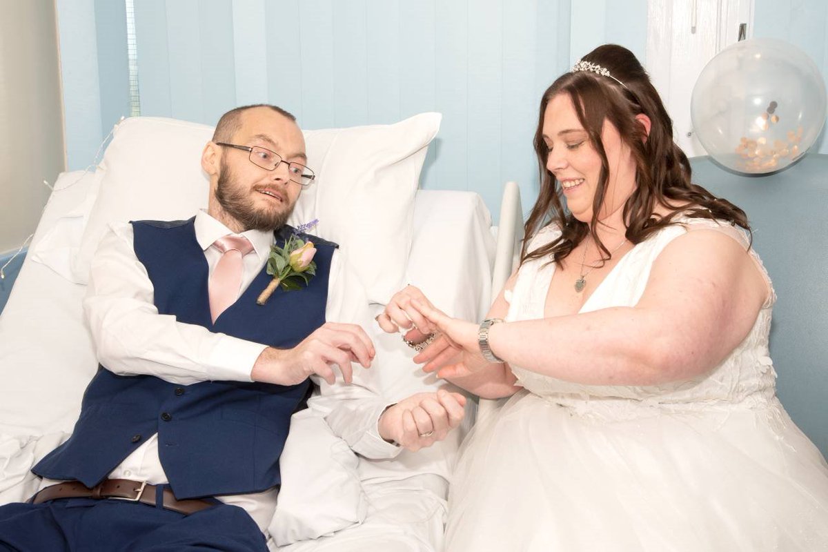 Patient Martin McMullan wearing a suit in his hospital bed as he exchanges rings with new wife Lindsay, who is wearing a white wedding dress.