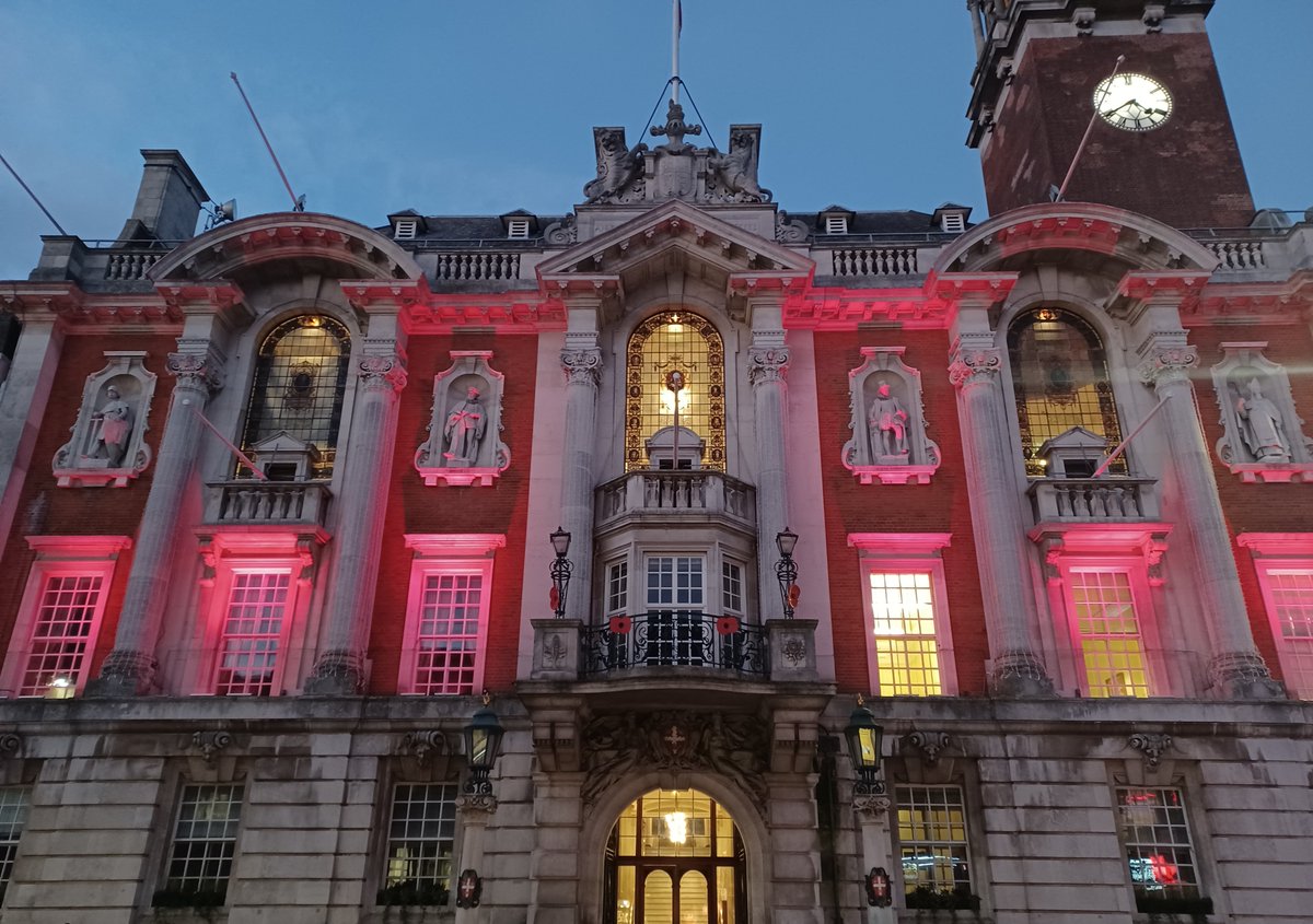 A photo of Colchester Town Hall lit red at dusk, with large red poppies on the Town Hall balcony in memory of those who lost their lives in conflict.
