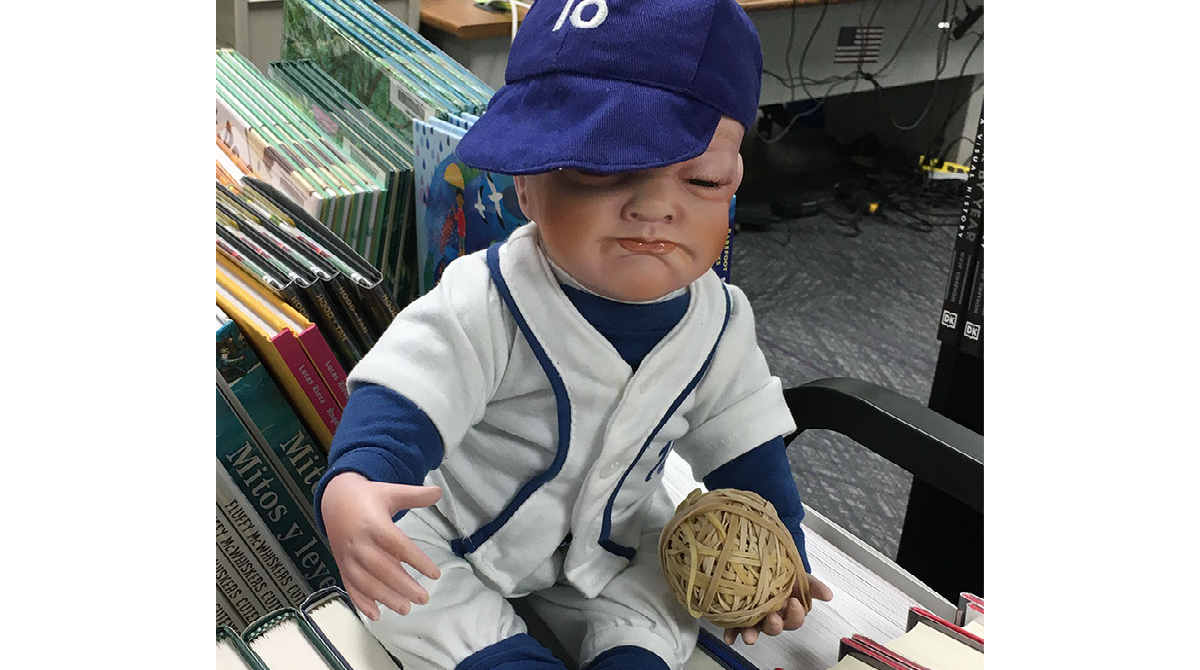 StChLibrary's tweet photo. Nigel, the resident #scarybaby in the Collections Services dept, was missing for several days. When he reappeared, it seemed that he had been enjoying...the World Series? We never know where Nigel will pop up! #wheresNigel #collserv https://t.co/E9TS0C2E4H