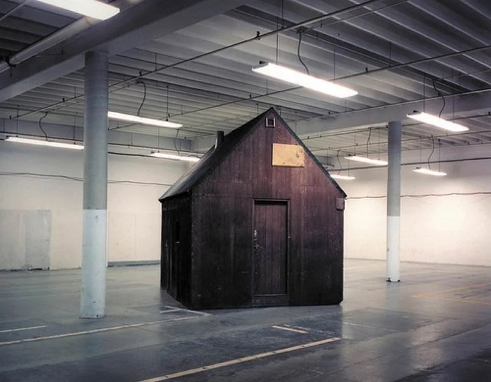 Dyslexeon's tweet photo. The following picture of Theodore Kaczynski’s cabin being held in a Sacramento Air Force Base is a work of fiction. The current whereabouts of said cabin are unknown. According to field agents, it “walked off” while it was being prepped for transport. https://t.co/u6D7ZrJqKs
