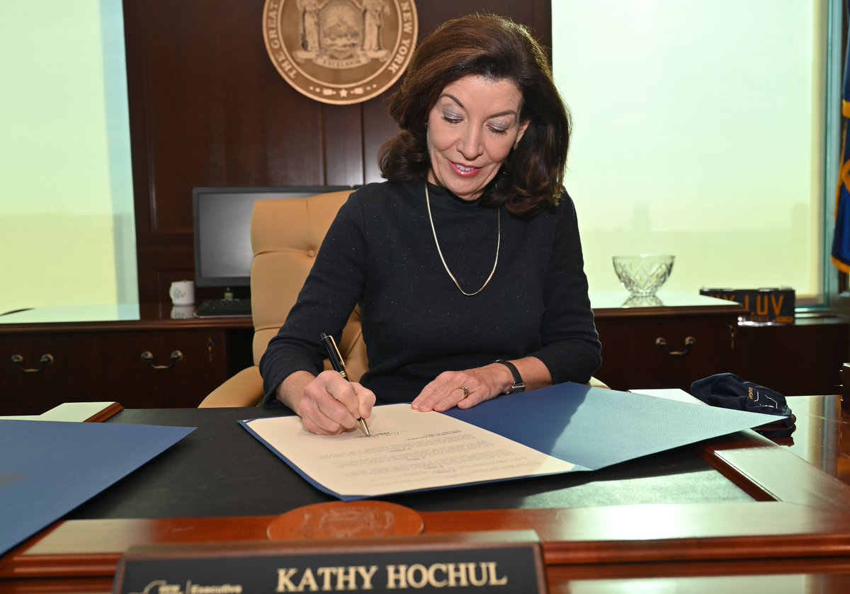 Governor Hochul sits at desk signing bill
