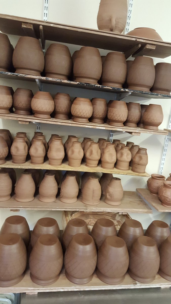 In the Potted History workshop. Shelves full of drying replica Roman pottery, in preparation for a firing of the replica Roman Pottery kiln at Vindolanda. Brown coloured jars with a burnished lattice pattern.