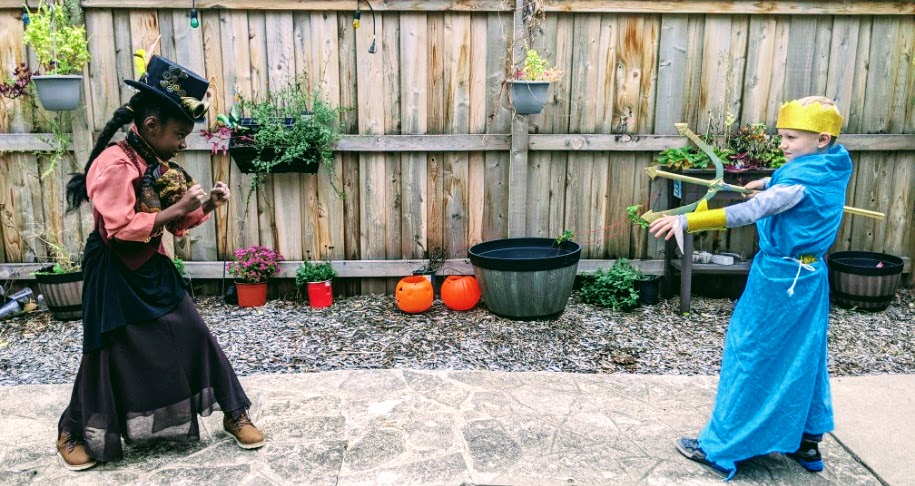 Black girl dressed in steampunk costume facing off with white boy dressed as Poseidon. Girl is posed with fisticuffs and boy is pointing trident at her.