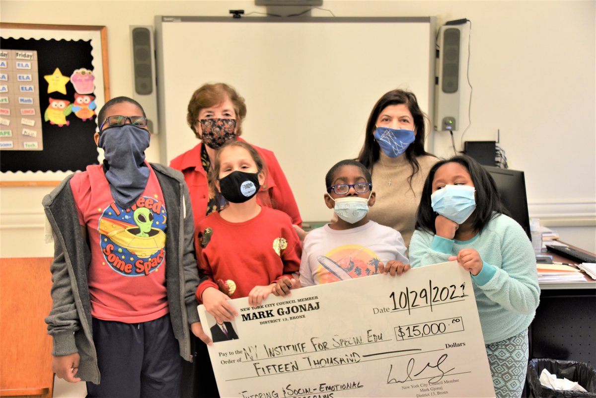 2 adults pose with 4 students,holding a large check. 