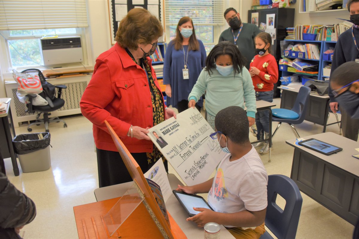 A teacher holds a giant check up to elementary students for them to see. 