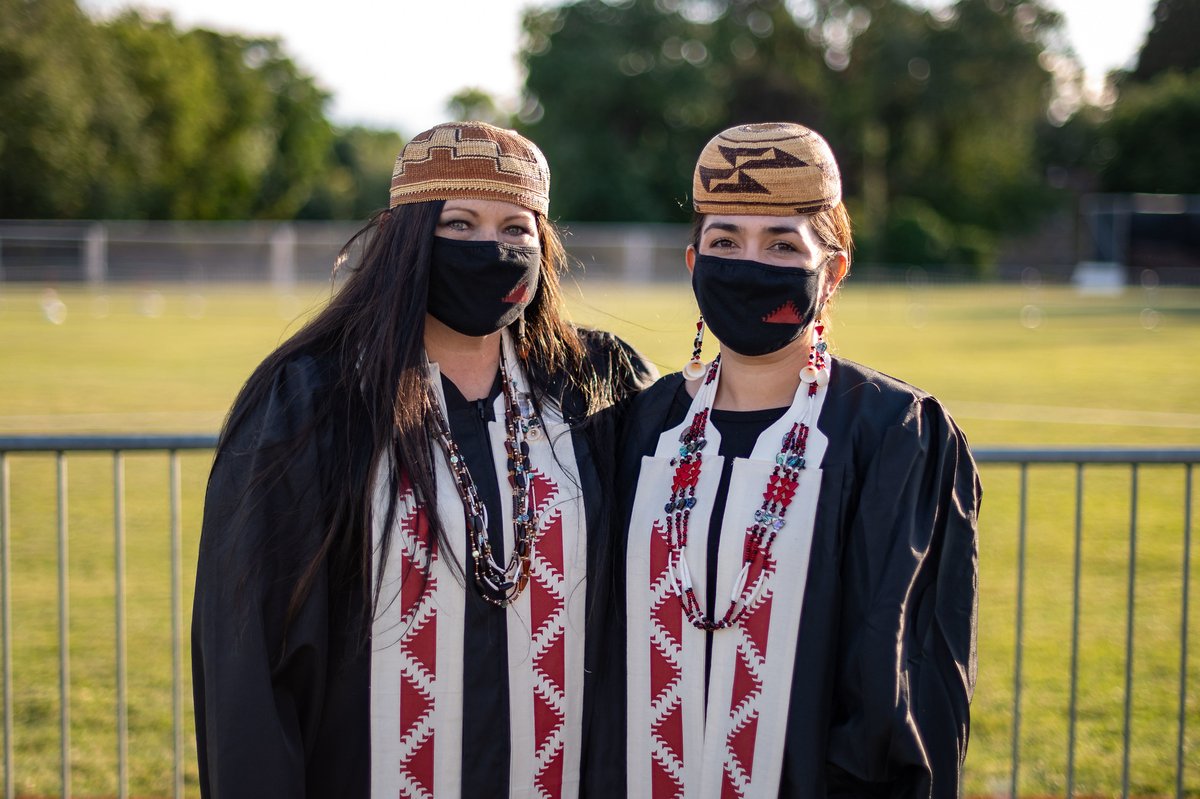 Two people wearing graduation gowns and tribal hats and sashes