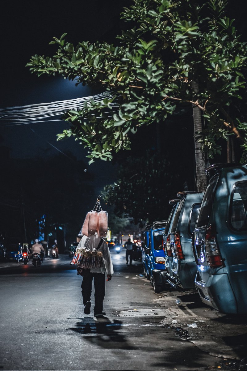 Menjelang pukul 10 malam, seorang penjual kapas gulali masih meneruskan langkahnya menyusuri jalan Bendungan Hilir, sesekali berhenti mengistirahatkan kaki, melalui penjual pulsa.