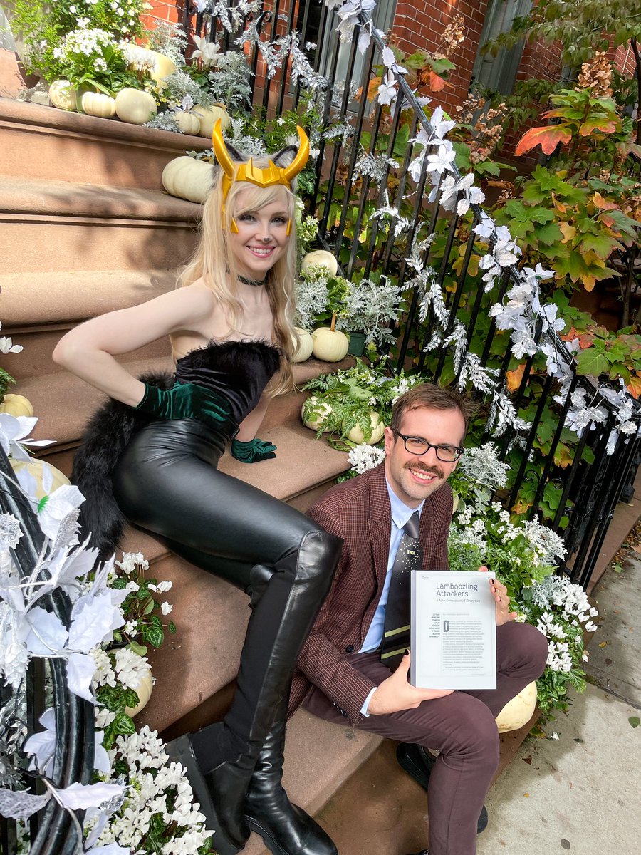 A picture of Ryan Petrich and Kelly Shortridge. Kelly is dressed in costume as a Loki-kitty variant, also known as “Lokitty”, and Ryan is dressed as Agent Mobius. They are holding a tablet that reads “Lamboozling Attackers: A New Generation of Deception”, a recent paper they published in ACM Queue.