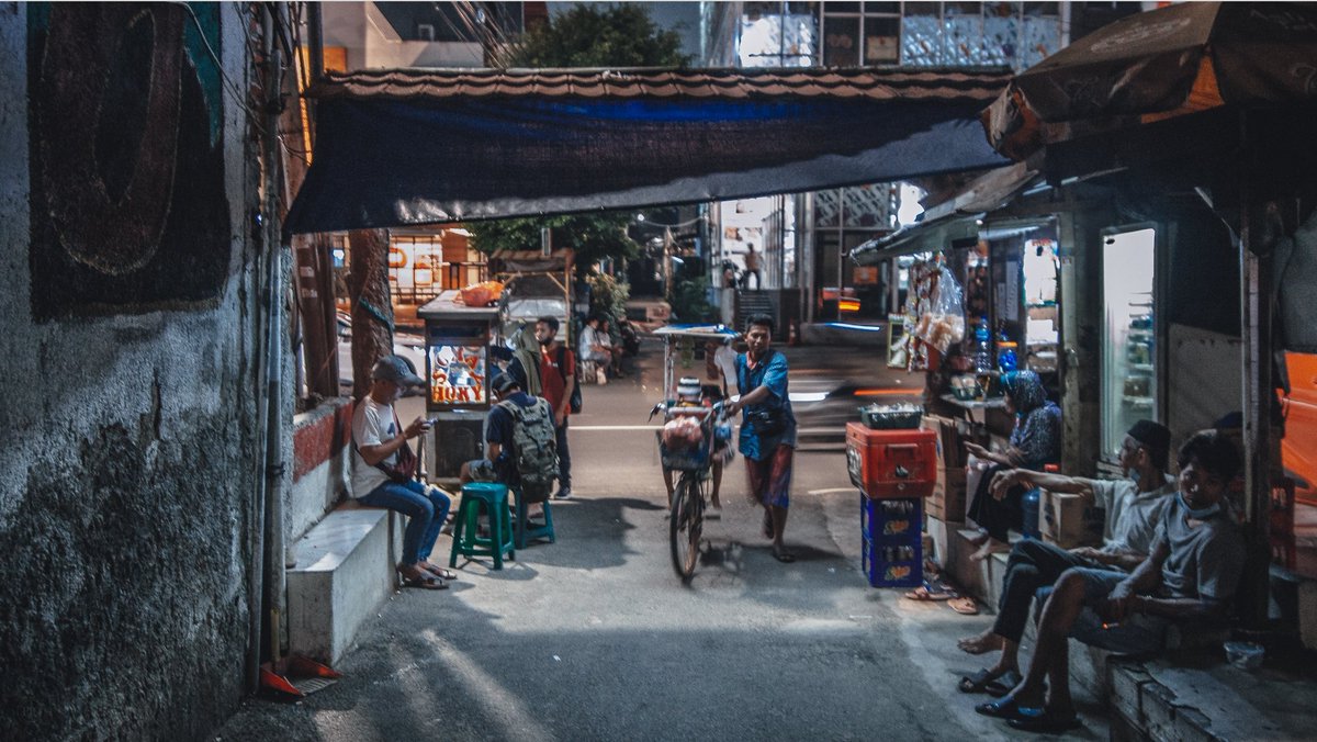 Salah satu gang di Benhil, berlatar belakang gedung tinggi yang tampak bercahaya di beberapa lantai meski di hari Minggu. Ada yang sedang lembur di salah satu ruangan ber-AC itu, sementara di sisi lain ada juga sedang lembur berjualan dari gang ke gang.