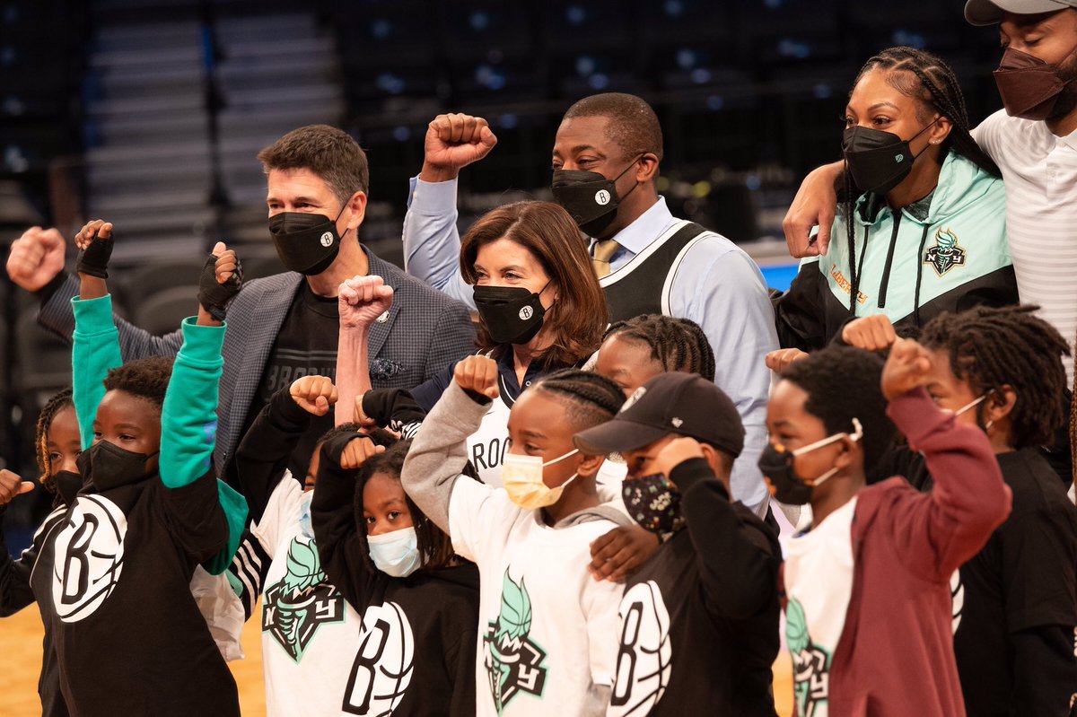 Governor Hochul stands masked with group of kids with arm raised