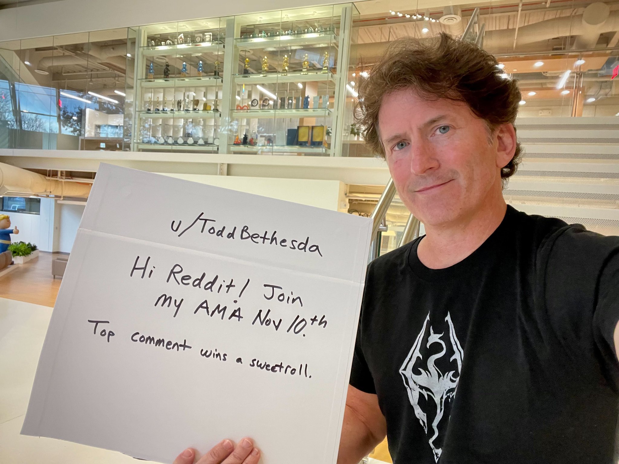 Image of Todd Howard holding up a sign that reads "u/ToddBethesda Hi Reddit! Join my AMA Nov 10th Top comment wins a sweetroll."