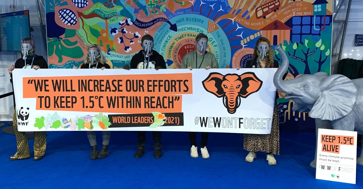 People in elephant masks hold a large banner with text showing a quote from world leaders reading 'We will increase our efforts to keep 1.5C within reach'