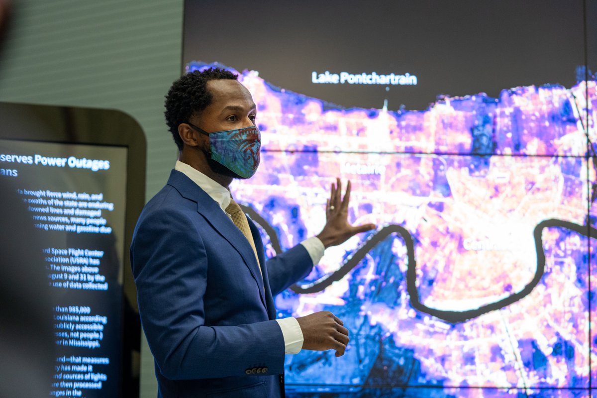 Dr. Christian Braneon standing in front of a screen showing a data visualization of New Orleans, gesturing at the image