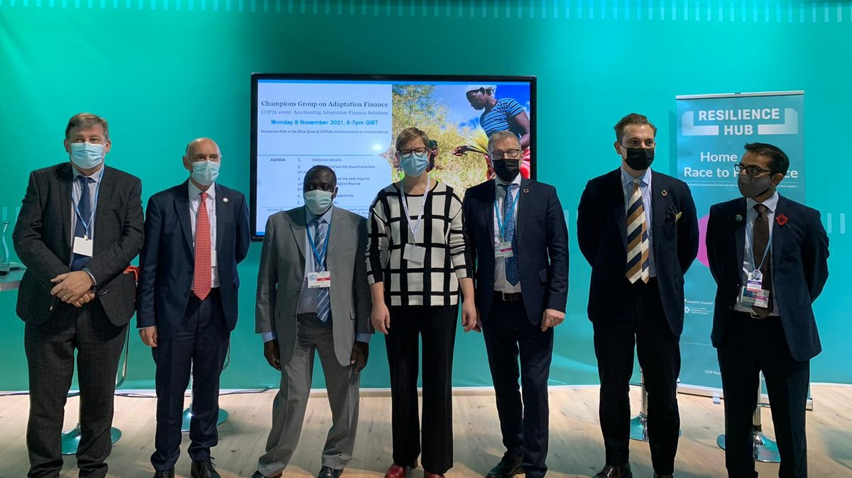 Six men and one woman wearing masks line up for a group photo on a stage.