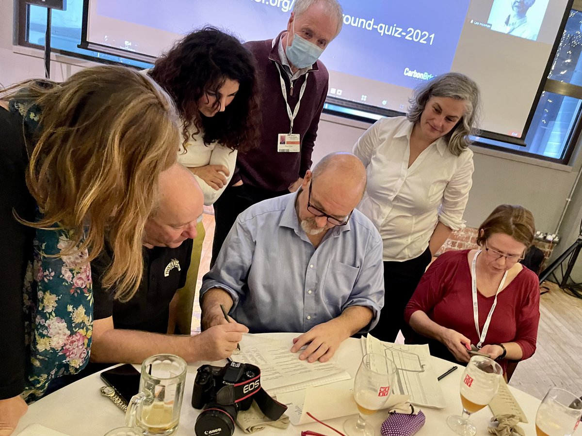 Group of quizzers pore over answer sheet in a huddle such as you get at COP climate negotiations.