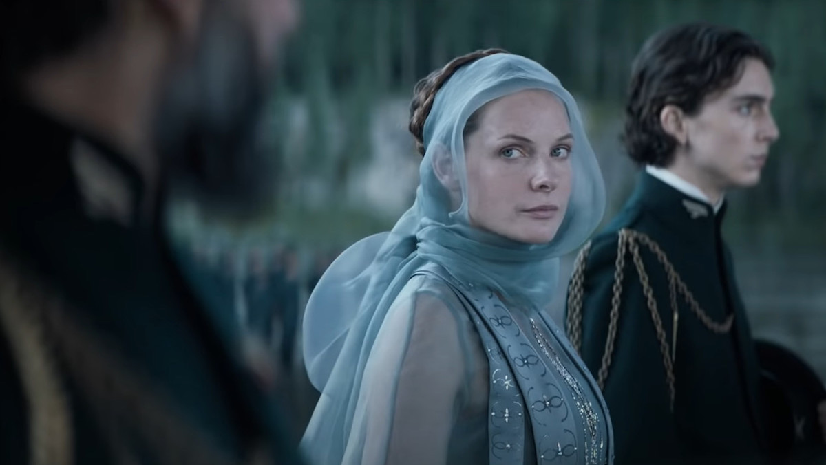 Rebecca Ferguson as Lady Jessica in blue sheer material and an embroidered blue gown beside Timothée Chalamet as Paul Atriedies in DUNE (2021). © Warner Brothers Pictures