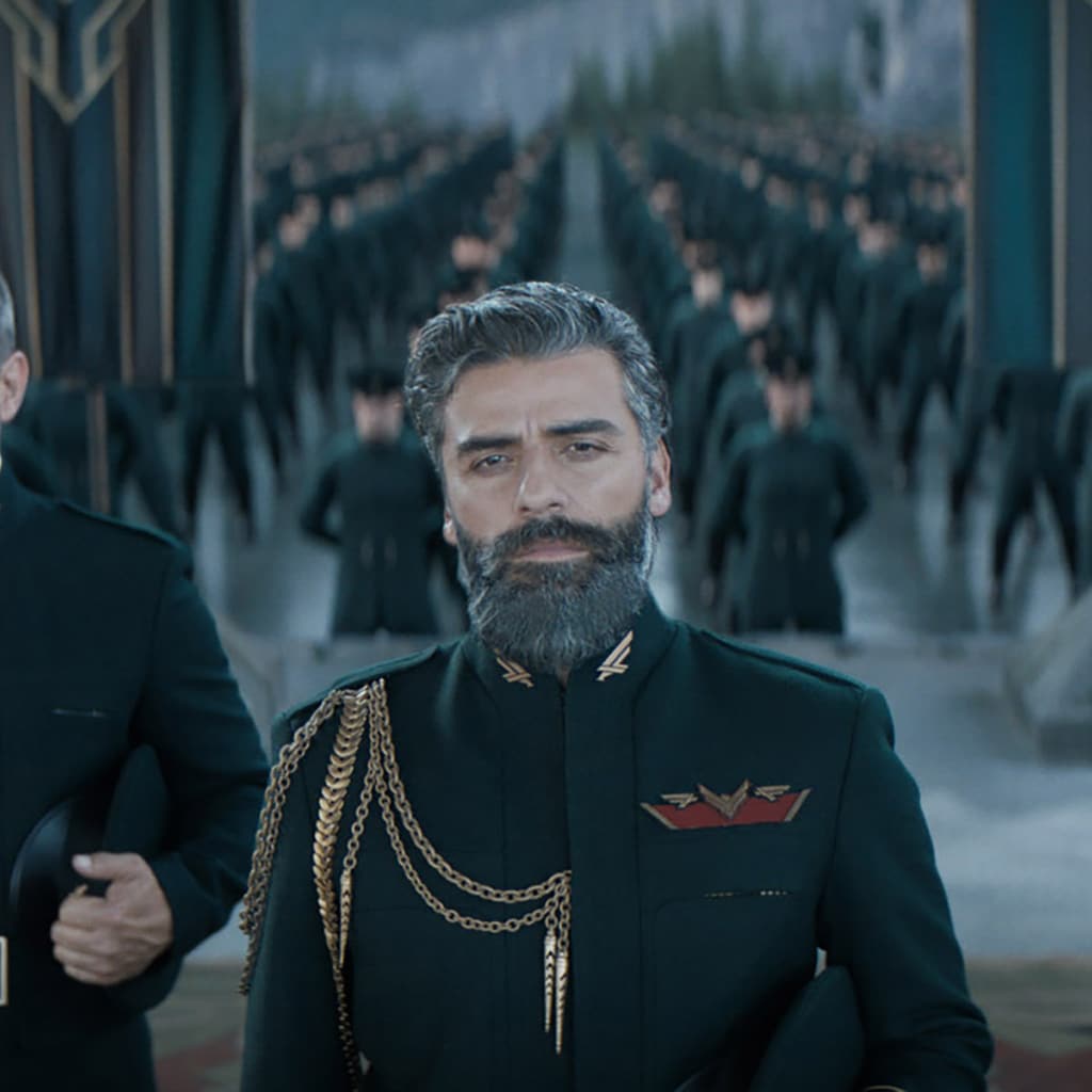 Oscar Isaac as Leto in DUNE (2021) wearing a black military suit with gold chains and pins, guards behind him. © Warner Brothers