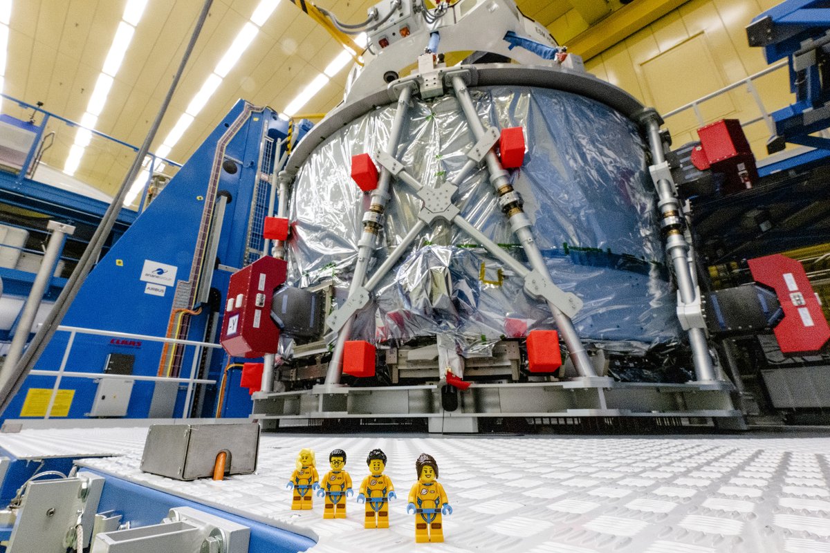 Four LEGO minifigures stand in front of European Service Module that will power the Orion spacecraft.