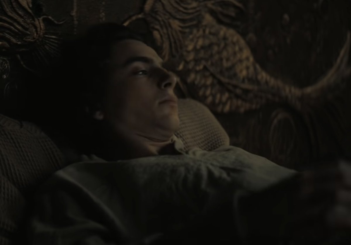Timothée Chalamet in DUNE (2021) waking from a bad dream in his gilded bed, wearing a white flax tunic. © Warner Brothers