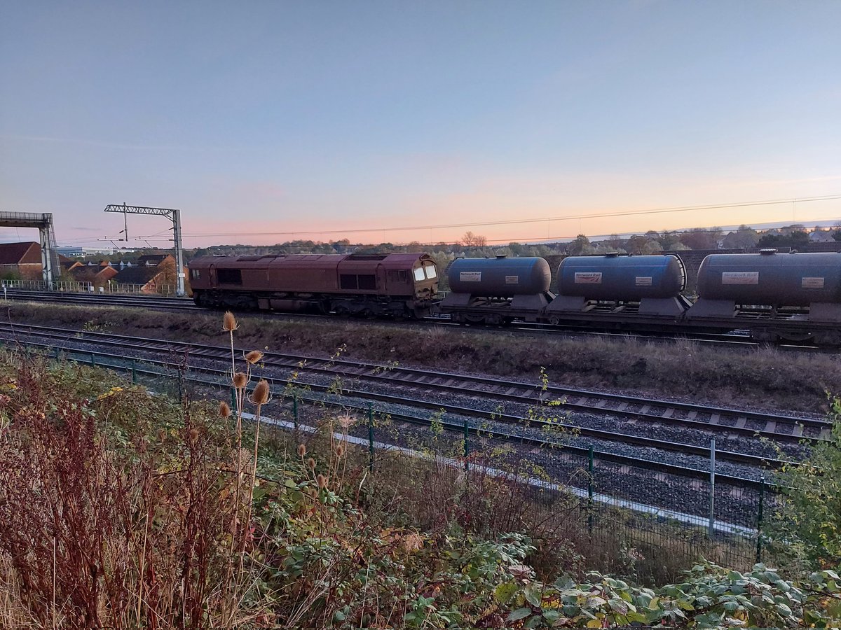 holtona72's tweet photo. A bright sunrise this morning over Kettering. 3J92 Toton-West Hampstead RHTT waits at north junction for the road across to the mainline from the down slow. Think this is probably 66111 &amp; 66174. No sign of #TreeCam this early! @Richphillips50 #ShedWatch #MML #Class66 9/11/21 https://t.co/X9xW2jFyPB