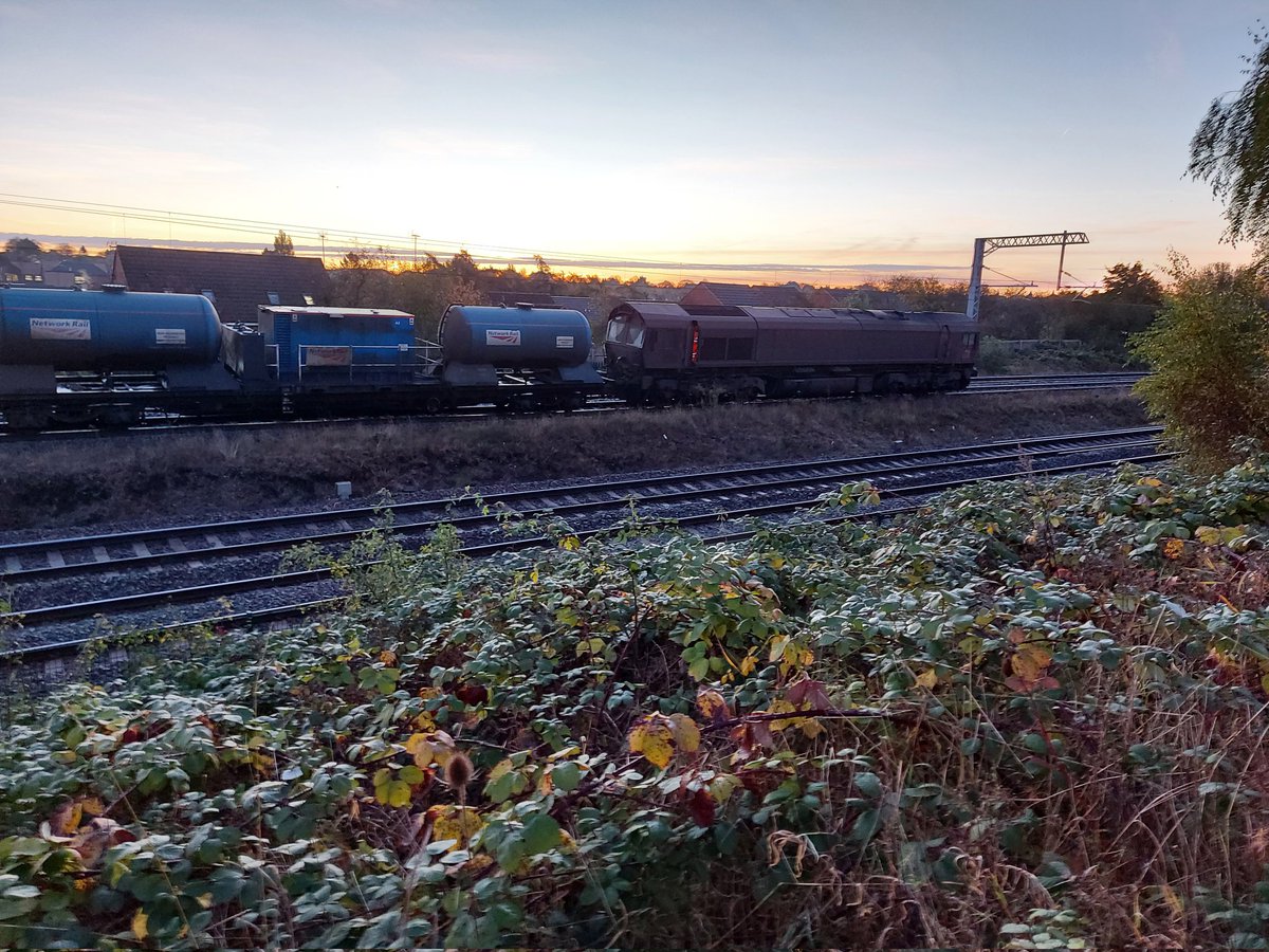 holtona72's tweet photo. A bright sunrise this morning over Kettering. 3J92 Toton-West Hampstead RHTT waits at north junction for the road across to the mainline from the down slow. Think this is probably 66111 &amp; 66174. No sign of #TreeCam this early! @Richphillips50 #ShedWatch #MML #Class66 9/11/21 https://t.co/X9xW2jFyPB