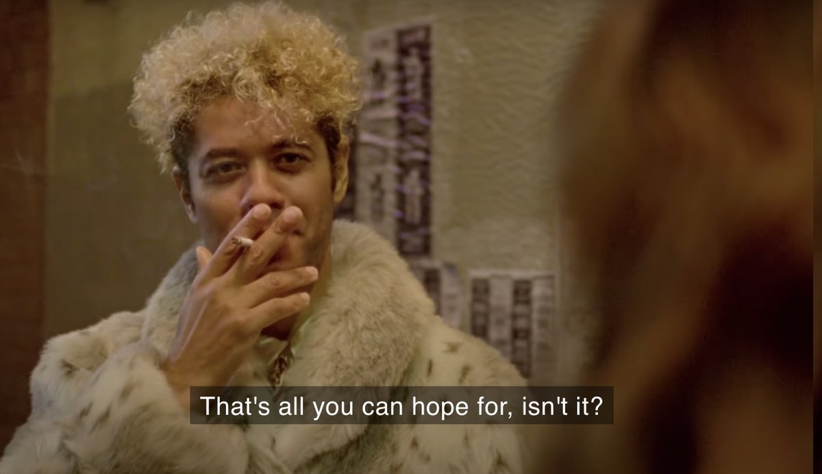 A man in an alleyway wearing a fur coat smoking a cigarette. Caption: "That's all you can hope for, isn't it?"