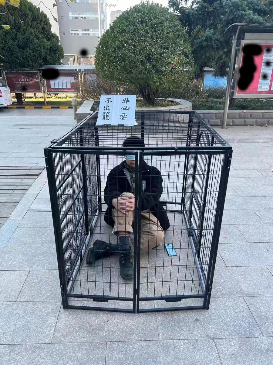 HoesomeChina's tweet photo. A performance art piece created by a student of the Beijing Film Academy went viral on Weibo but disappeared quickly. In the piece, a student is trapped in a cage with a mask covering his eyes, and a card above the cage reads "Don't get out of the cage unless necessary". https://t.co/n6KHYETCq7