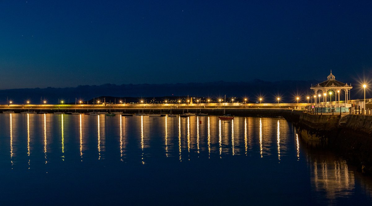 edgecases_urban's tweet photo. Twilight at the West Pier, Dun Laoghaire. The air was completely still, so the reflections of the lights are almost perfectly straight in the water, and the dark mass of Howth looms behind, illuminated by the stars above.

https://t.co/j3HF8n2LSt https://t.co/McEvSi6pDm