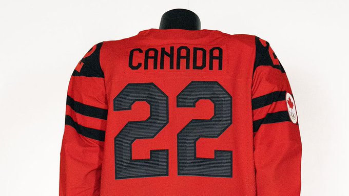 A Canadian hockey jersey on a headless mannequin. The jersey is red with the word Canada in capital letters across the back in black. The number 22 in black in the middle back of the jersey. The beginning of two thick black stripes coming out from the number 22. Two thick black stripes around the upper arm area.