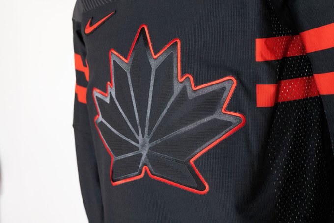 A close up of a black Canadian hockey jersey. A black maple leaf with a red outline around it on the jersey. 