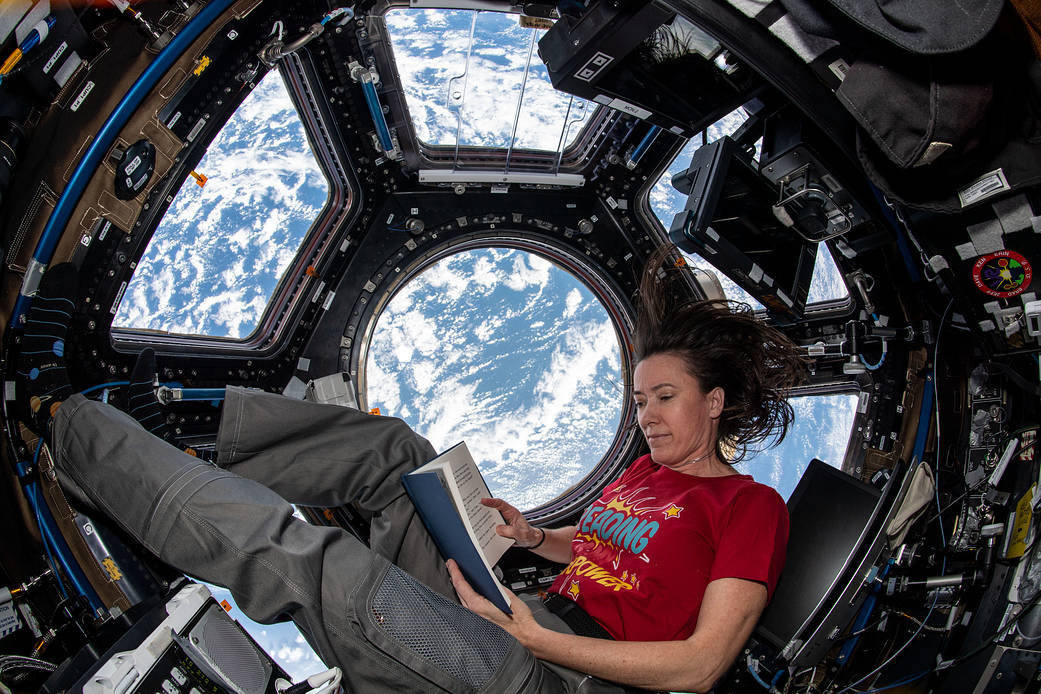 Astronaut Megan McArthur reads a book while floating inside the cupola of the space station 