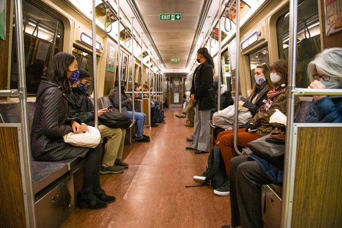 Michelle sits on the T and speaks across the aisle to two seated women.