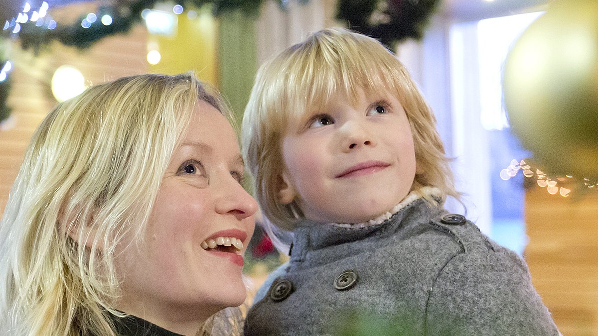 Colour photo of a woman holding a small boy looking at festive decorations.