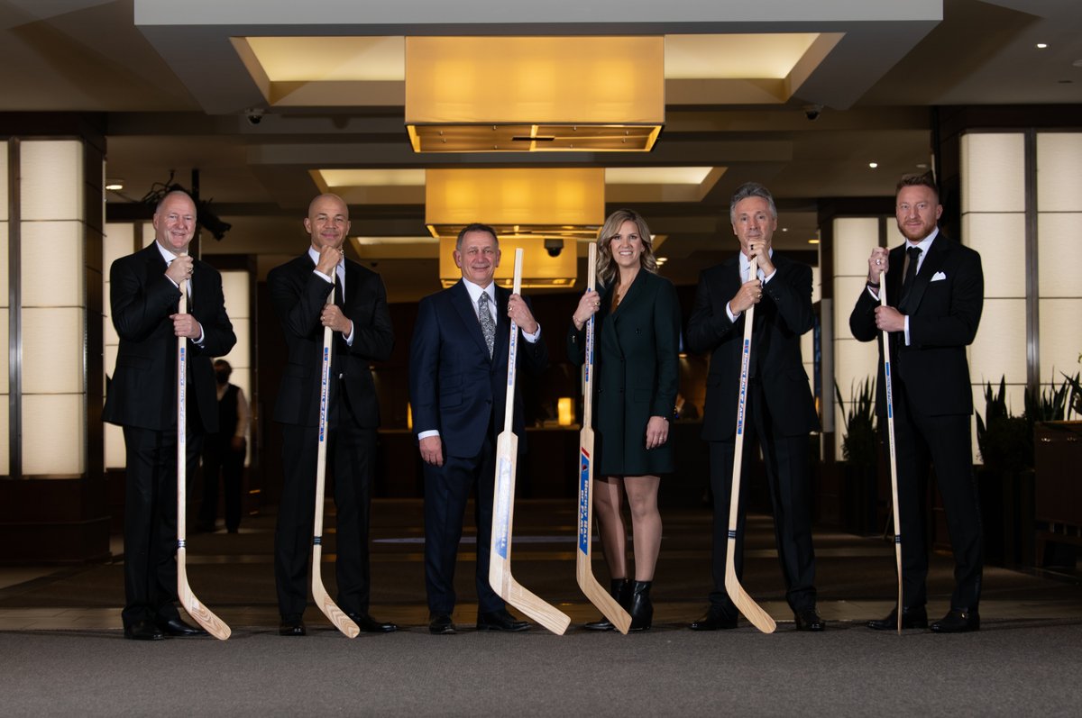Kevin Lowe, Jarome Iginla, Ken Holland, Kim St-Pierre, Doug Wilson and Marian Hossa stand side by side holding wooden sticks. Photo credit: Matthew Manor/HHOF