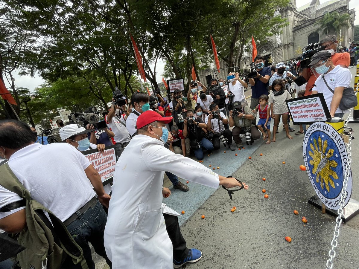 Joseph_Morong's tweet photo. Members of Nurses United Partylist pelt the COMELEC logo with tomatoes to denounce denial of accreditation @gmanews https://t.co/q7jXnHpAVS