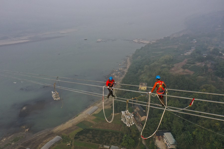 PDChina's tweet photo. "Spider men" in action: Photos taken on Dec. 5, 2021 show utility technicians working on a power transmission project at a height of about 100 meters above the Yangtze River in southwest China's Chongqing. https://t.co/8D493mS1vc