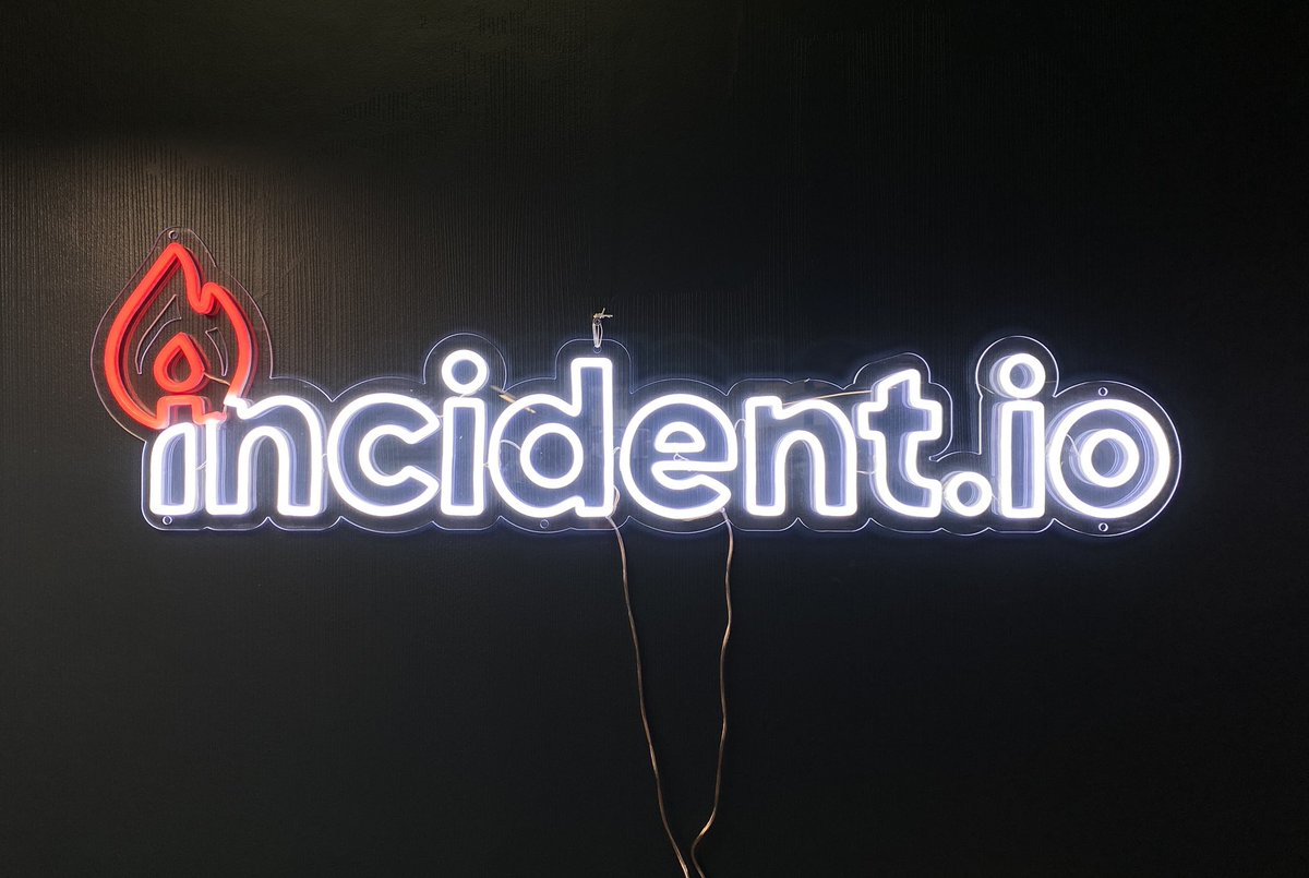 A neon sign featuring the incident.io logo in white, and a red flame on the first I.