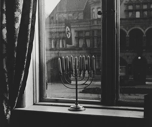 In 1931, across Rabbi Posner’s home, stood the Nazi headquarters. Rabbi Posner’s wife Rachel lit the Menorah, capturing the Nazi flag in the background. 

On the back of the photo she wrote, “Our light will always outcast their flag.”

To all celebrating #ChagSameach #Hanukkah