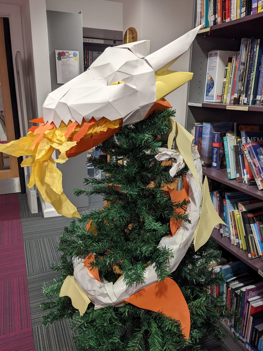 Library_EHS's tweet photo. A dragon in the library xmas tree?! Why not? I think this fierce creature needs a name. Write down your suggestions on the whiteboard and whoever's name gets picked will earn a prize! #dragon #xmastree #librarydisplay #holidaydecor https://t.co/agrIJB7vsB